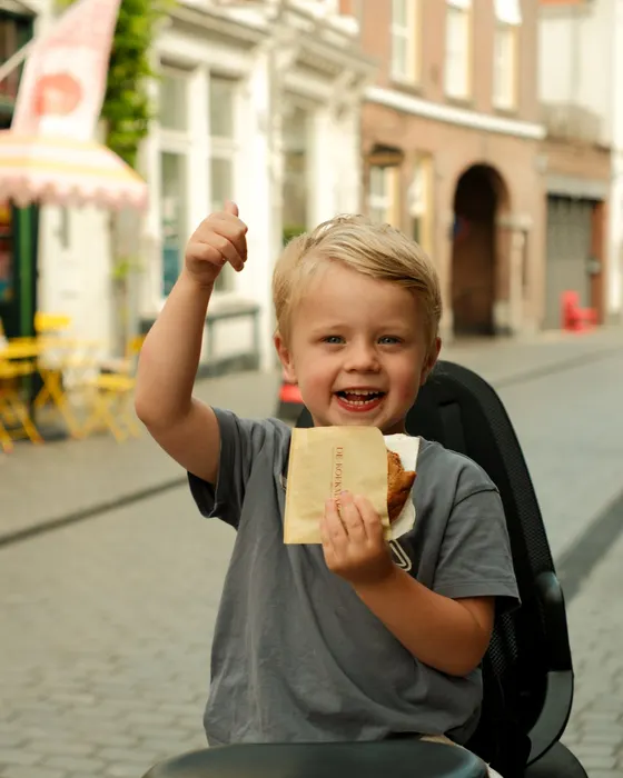 Een lachend jongetje met een zakje van De Koekmakerij