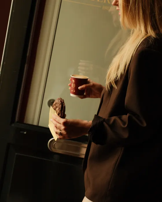 Een gast loopt met koffie en een koek de winkel uit